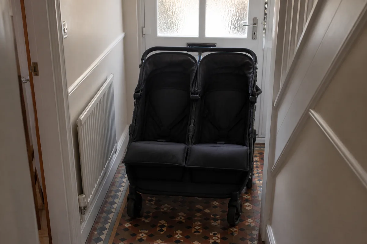An empty two-seat pushchair in a narrow UK hallway by the front door