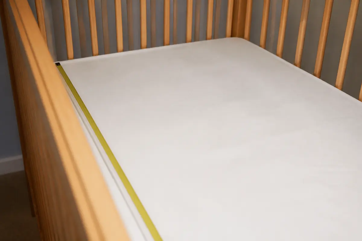A firm cot mattress with a waterproof cover and a tape measure along the edge