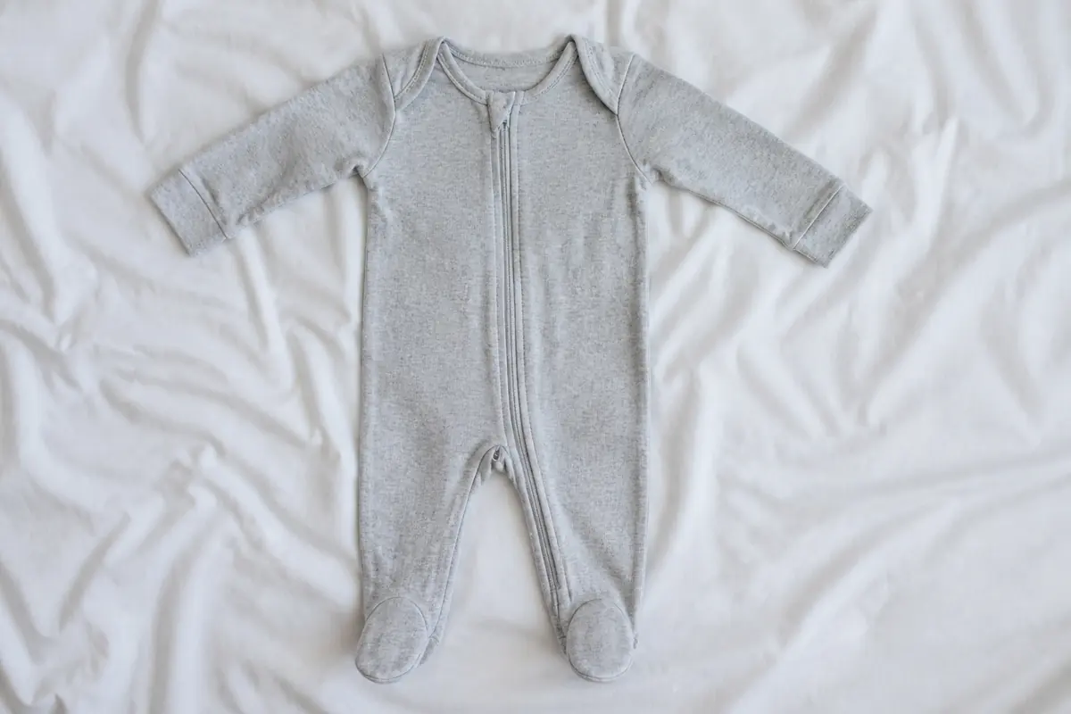 A single zip sleepsuit laid flat on white sheets, envelope neck visible